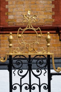Decorated black and gold painted iron gate in front of a brick wall, Chelsea, London, Great