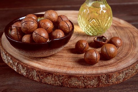 Bottle of macadamia oil, on a wooden board, with macadamia nuts, wooden background, selective
