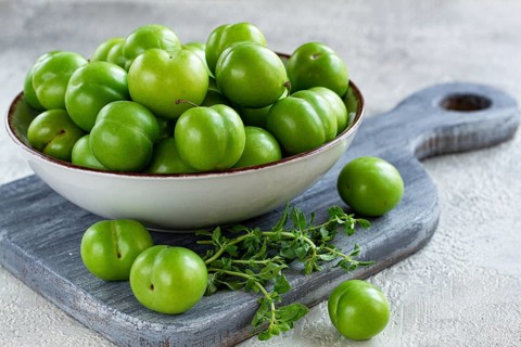 Tkemali, green cherry plum, in a bowl, on a gray table, top view, natural light, no people