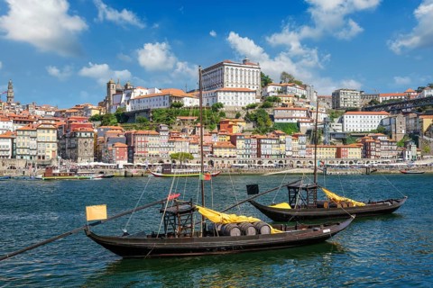 Rabelo boats on Douro River by Porto Ribeira with visible wine company names, barrels and bridge