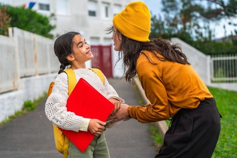 Mother and daughter interacting warmly, with the girl ready for school wearing a backpack and