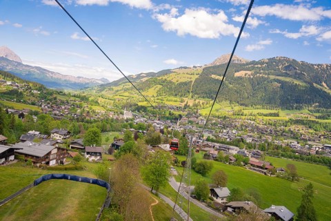 Cable car over a village with green meadows and forests, surrounded by mountain scenery,