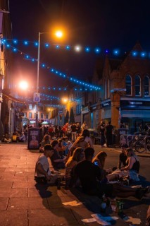 Group of people sitting on a street surrounded by warm lights and lanterns, nightlife, Dublin,
