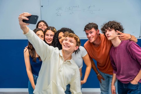 Happy multiethnic students gathering close together, smiling and posing for a group selfie in a