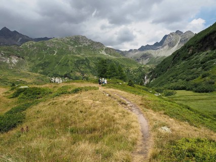 A hiking trail snakes through a mountainous landscape under cloudy sky, Binntal Landscape Park,