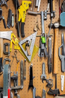 Various hand tools including axe, hammer, clamps, metal saw blades, keys hanging on light brown
