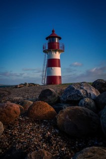 A red and white lighthouse stands on a rocky beach in the evening mood in calm skies, Grisetaodde