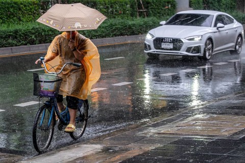 Female cyclist and passenger car in rain, Bangkok, Thailand