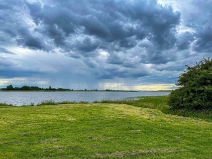 A vast landscape with cloudy sky over a lake and grassy area, Ummanz, Mecklenburg-Western