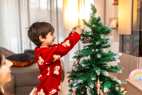 Young boy in red pajamas helps his mother hang ornaments and pinecones on the christmas tree,