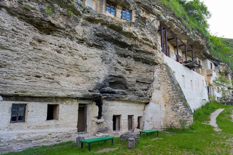 Historic façade of a cave monastery with green benches and several windows, rock caves, cave
