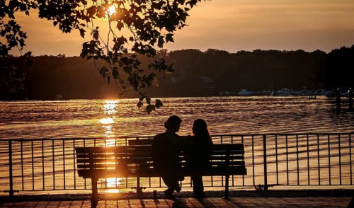 Silhouette in sunset, a couple sitting romantically on a bench enjoying the sunset on the water,