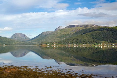 A calm lake with reflections of the mountains and the sky. Small settlement in the background,