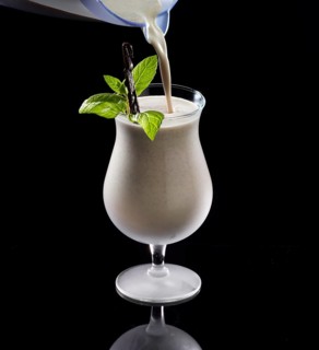 Light brown cocktail is poured against a black background, mint and vanilla bean as garnish, studio