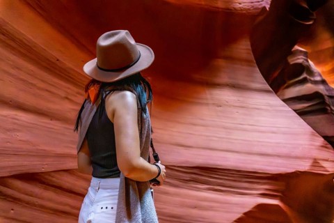 Woman in a hat looking at the illuminated, winding sandstone walls of antelope canyon, a famous