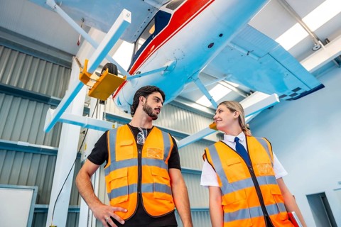 Two aviation professionals male mechanic and female pilot in high visibility vests stand in a clean
