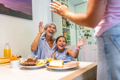 Happy grandmother and granddaughter sitting at a kitchen table, smiling and raising their hands