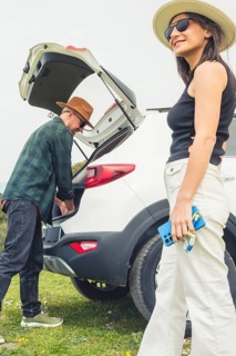 Excited Traveling couple packs puts big luggage to white rented SUV vehicle trunk on scenic