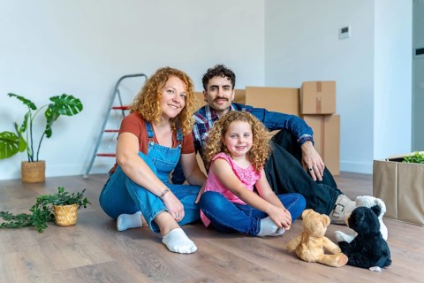 Cheerful family with a young daughter celebrating moving into their new house, sitting together on