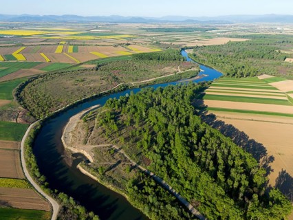 The river snakes through an extensive agricultural landscape with fields and forests on a sunny