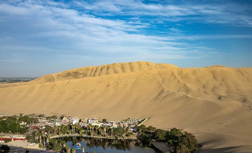 The oasis, Laguna Huacachina with a small lake and houses surrounded by sand dunes in the Ica