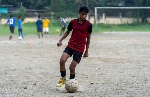 Children play football on a dusty neighbourhood field, chasing the ball with energy and