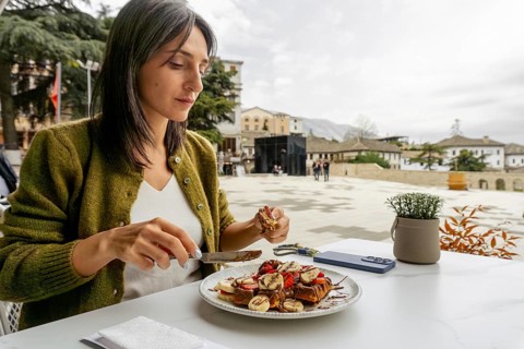 Close up woman sit in cafe enjoying large, indulgent waffle dessert portion topped with fruit and