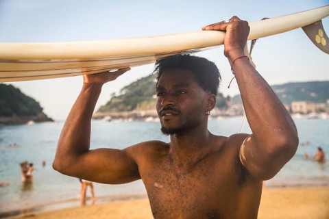 Young man standing on a sandy beach carrying a surfboard on his head, enjoying a summer day near