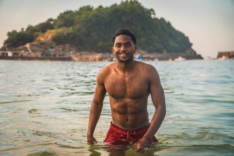 Young man smiling at camera while swimming in the ocean on a summer vacation, with an island in the