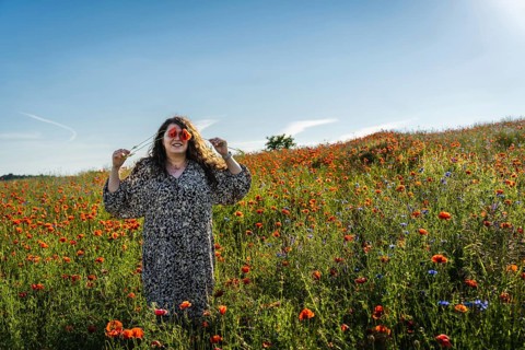 Plus size woman covering eyes with poppy (Papaver rhoeas) flowers while standing in blooming field