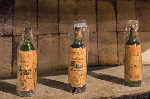 Three old wine bottles with labels and protective film in a historic cellar environment under light