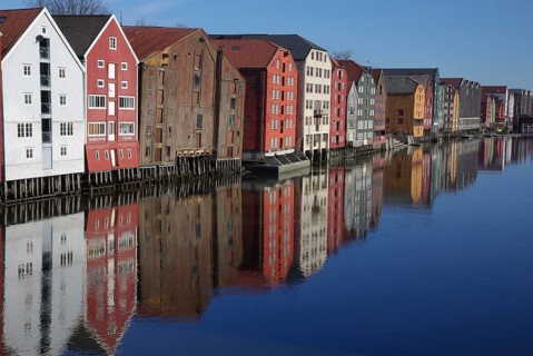 Row of colorful buildings reflected in calm water with clear sky, Trondheim, Nidelva, Tröndelag,