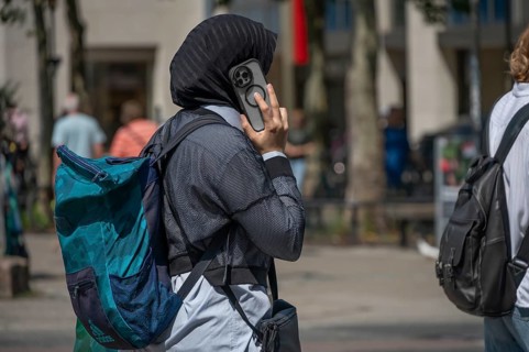 Young woman with headscarf and cell phone talking on the phone in the pedestrian zone, Bavaria,