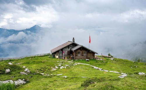 Small mountain hut Suls-Lobhornhütte with Swiss flag, cloudy mountain landscape, Bernese Alps,