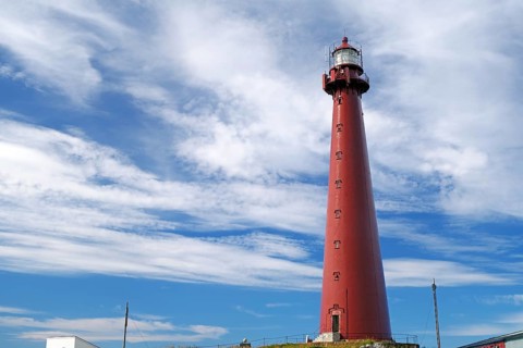 A tall red lighthouse with clouds in the sky in a coastal landscape, landmark, Andenes, Andøya,