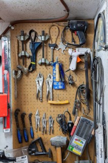 Various hand tools including vise grips, soldering and glue guns, sledge hammers hanging on light