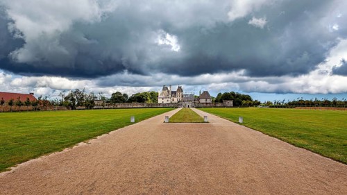 A castle in the distance with dramatic skies and dark clouds surrounded by lawns, Château de