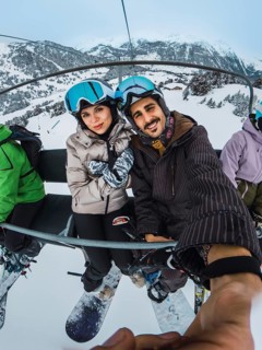 Happy young man and woman wearing snowboard gear, helmets, and goggles, smiling at the camera while