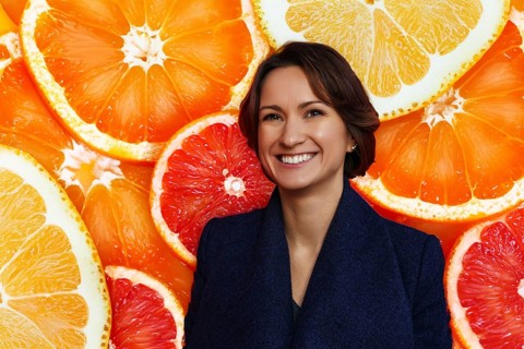 Smiling young woman in dark blue coat with citrus background