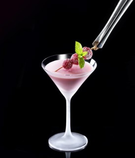 Red cocktail in iced glass against a black background, mint and raspberry skewer as garnish, studio