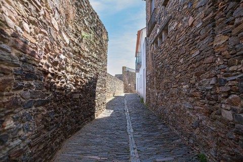 A shady, narrow alley between tall old stone walls, Monsaraz, Évora, Portugal