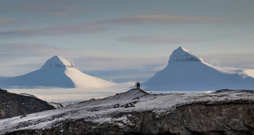 Two people, including a photographer with a stand in front of two of the three mountains Tee