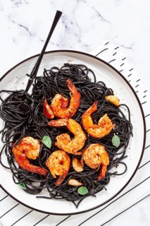 Black spaghetti with shrimp, on a white plate with a fork, on a striped napkin, marble background,