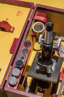 Stored vintage black Bausch & Lomb research microscope with objective lenses in opened brownish red