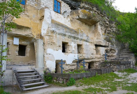 Entrance to a rock carved monastery with blue crosses and stairs under green leaves, rock caves,