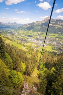 View from a cable car of a green wooded valley and mountains under a blue sky, Hahnenkamm,