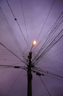 Power pole with numerous cables under a purple evening sky with a glowing lantern, Ecuador