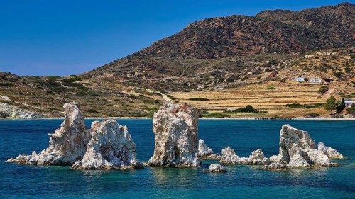 A series of rocks against a mountainous landscape and calm sea under clear blue sky, Aspragremna,