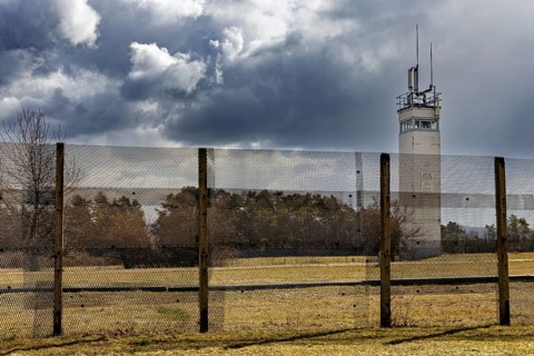 A high fence stretches out in front of a watchtower in a covered landscape, the Point Alpha