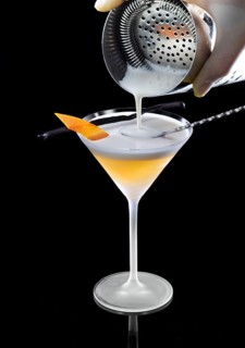 Orange-colored cocktail is filled with cream, against a black background, orange peel and vanilla